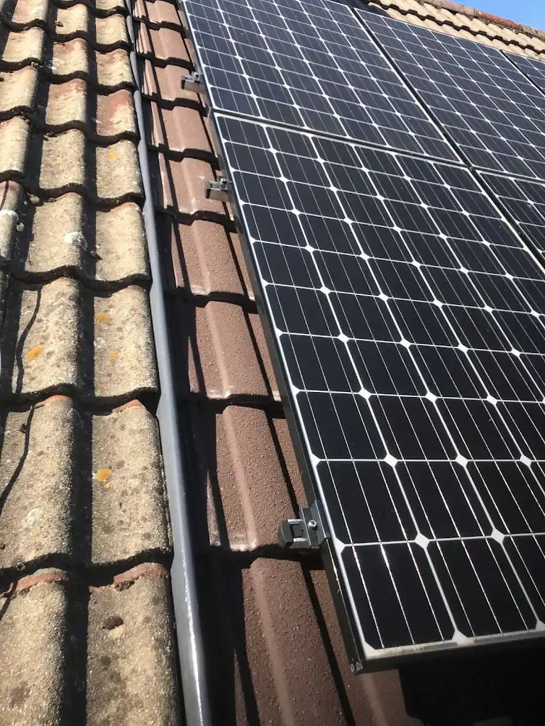 Close-up of solar panels installed on a rooftop with brown tiles under a clear blue sky. The panels are aligned parallel to the tiles, capturing sunlight for energy.